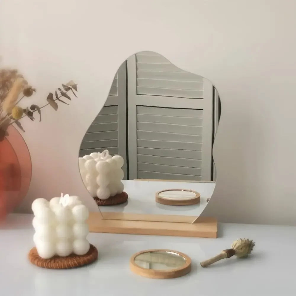 Freestanding irregular mirror with smooth reflective surface and wooden base on a dresser