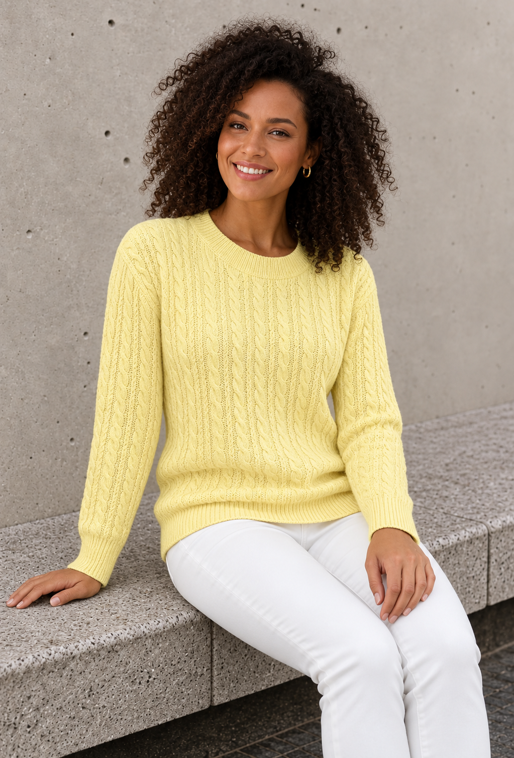 Women's pale yellow cable knit sweater with long ribbed-cuff sleeves, seated