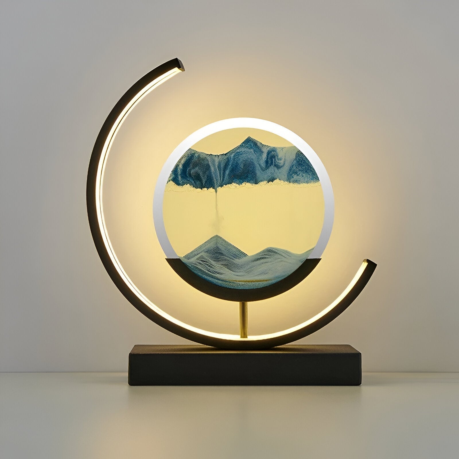 Rotating sand art lamp with glass enclosure and metal base on a flat surface
