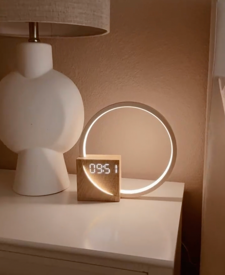 Digital clock lamp with wood-effect base and circular LED light ring on a desk