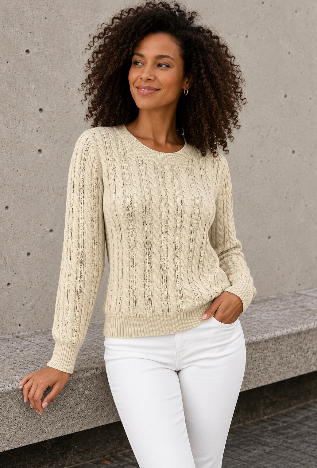 Women's light beige cable knit sweater with ribbed cuffs, hand in jeans pocket